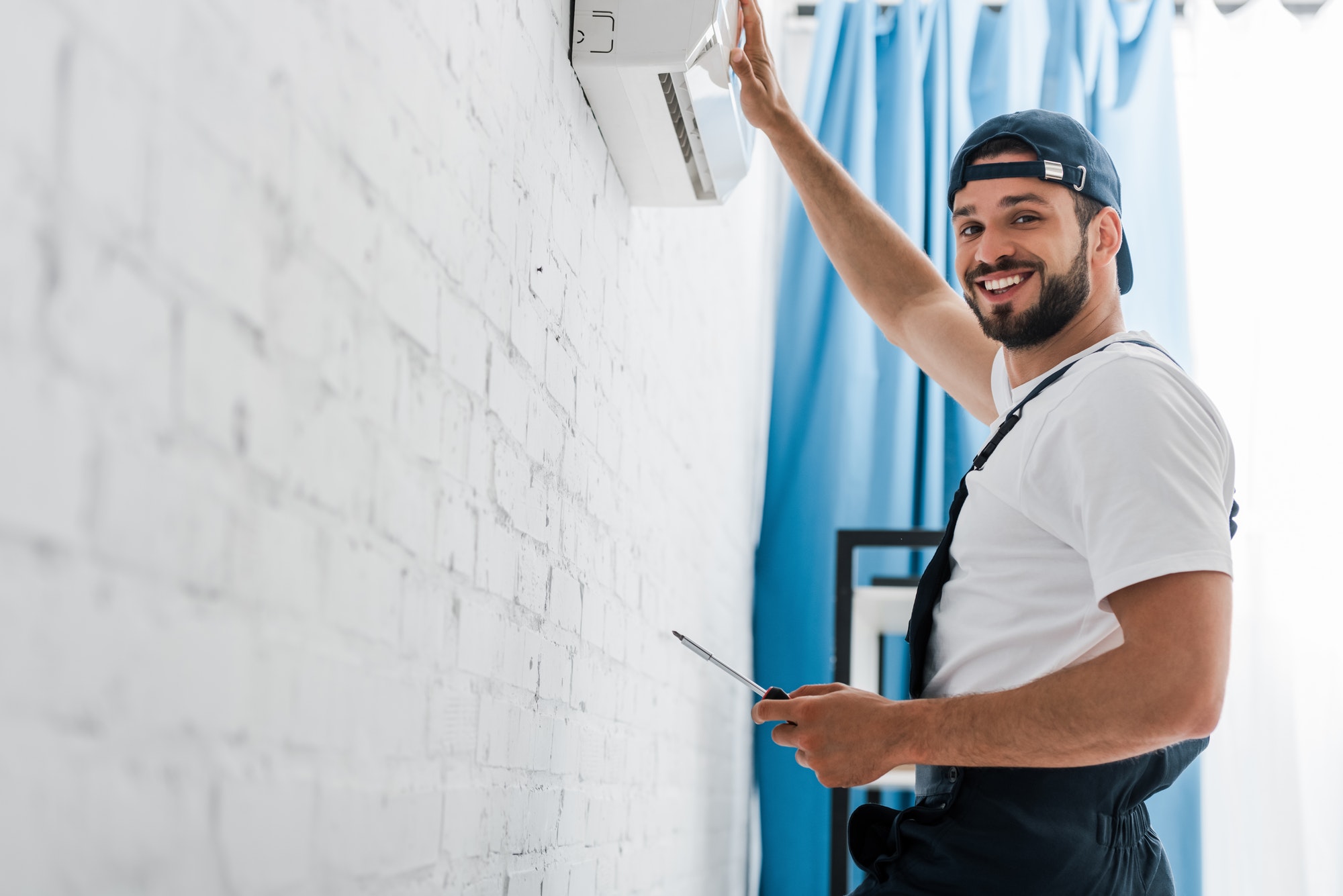 Smiling workman looking at camera while repairing air conditioner